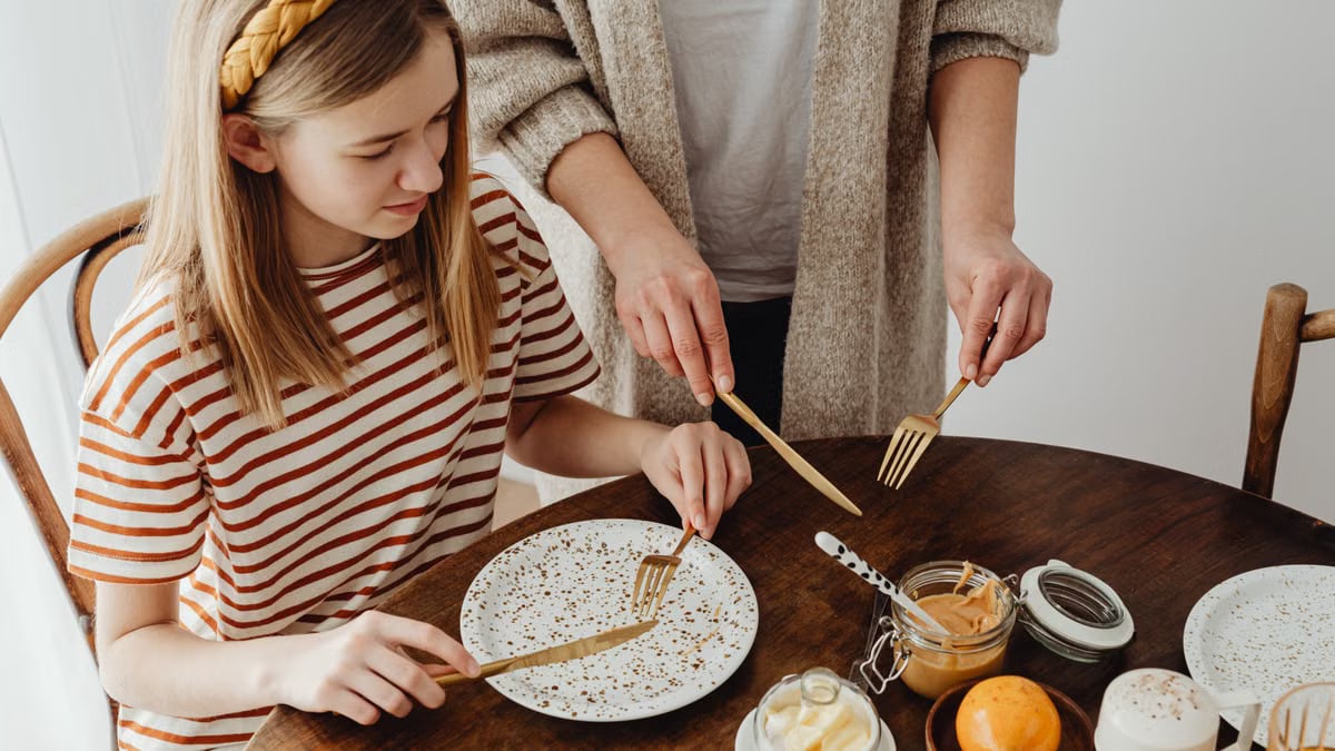 A teenager and adult at a cozy dining table with jars and wooden utensils.